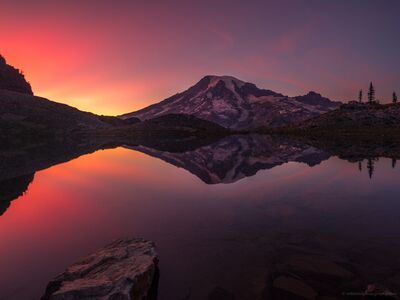 Mount Rainier Crimson Sunset Reflected in a Hidden Alpine Tarn A brilliant crimson and coral sunset illuminates the sky above Mount Rainier, reflecting in the perfectly still waters of a secluded alpine tarn near the...