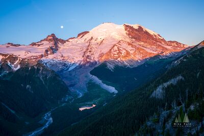 Mount Rainier Sunrise Alpenglow and Moon Above White River Valley Warm pink and golden sunrise light illuminates the immense glaciers and snow-covered summit of Mount Rainier, photographed from the Silver Forest Trail in the...