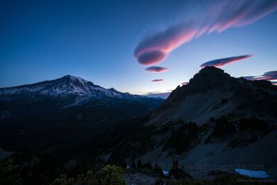 Sunrise Light on a Lenticular Vortex Above Mount Rainier At dawn, a vibrant lenticular vortex cloud glows above Mount Rainier, its edges brushed with the soft pink light of sunrise. The mountain’s icy slopes and...