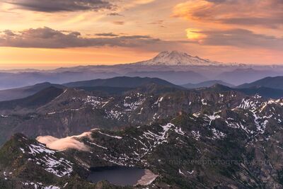 Mount Rainier Beyond Norway Pass at Sunset An aerial view across Norway Pass in the Mount St. Helens region of Washington, looking north toward distant Mount Rainier. Rugged, snow-streaked ridges and a...