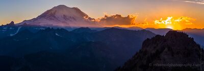 Northwest Aerial Photography Rainier Sunset Above Yakima Peak A panoramic aerial view of Mount Rainier at sunset, glowing in fiery hues above the rugged Cascade Range. The sun dips below the horizon, casting dramatic light...
