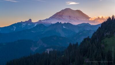 Northwest Aerial Photography Rainier Sunset From Tipsoo A serene evening view of Mount Rainier from Chinook Pass as the last light of sunset brushes the Cascade ridges in warm tones. Layers of blue ridgelines and...