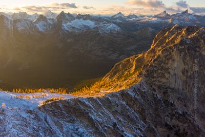 Over the Northwest Larches and Early Winters Aerial Golden sunset light sweeps across snow-dusted ridges and glowing alpine larches near Washington Pass in Washington’s North Cascades. Captured by Mike Reid...