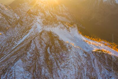 Over the Northwest Larches and Peaks Sunset Aerial view of the North Cascades bathed in golden sunset light as alpine larches glow along snow-covered ridges. Captured by Mike Reid Photography, this fine...