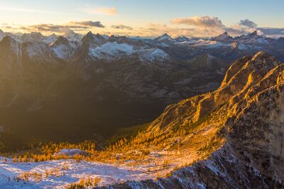Over the Northwest North Cascades Aerial Larches An aerial sunset view over Washington Pass in the North Cascades, where golden light illuminates snow-dusted larches and rugged granite ridges. Captured by Mike...