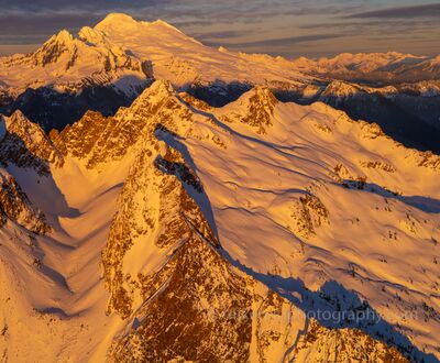 North Cascades Sunset Alpenglow Over the Sisters Range and Mount Baker Brilliant golden-orange sunset light illuminates the snow-covered peaks of the Sisters Range in Washington's North Cascades, with Mount Baker rising...