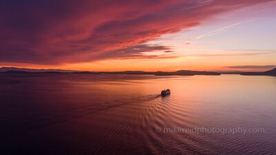 Northwest Aerial Photography San Juan Islands Ferry Peaceful Tranquility.jpg A peaceful aerial view of a Washington State ferry gliding across Puget Sound toward the San Juan Islands under a vivid red and orange sunset sky. The evening...