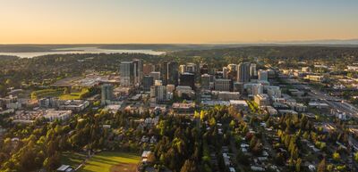 Over Bellevue Aerial Drone Evening Light Aerial evening view over downtown Bellevue, Washington, with the city’s modern skyline rising above tree-lined neighborhoods in warm golden light. Lake...