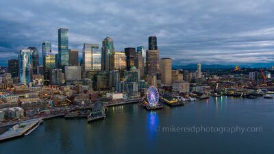 Over Seattle Blue Hour Skyline A serene aerial view of Seattle’s downtown waterfront as dusk settles over Elliott Bay. The city’s skyscrapers glow with reflected light beneath a moody sky,...