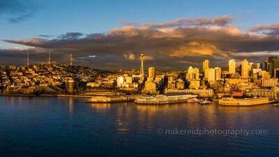 Over Seattle Space Needle Golden Light A striking aerial photograph of Seattle’s Space Needle and waterfront glowing in the rich light of sunset. The city’s architecture is bathed in deep golds and...