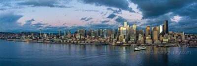 Over Seattle at Dusk Ferry Arriving Panorama A panoramic aerial view captures Seattle’s skyline as a Washington State Ferry glides into Elliott Bay under a dramatic evening sky. The Space Needle rises...