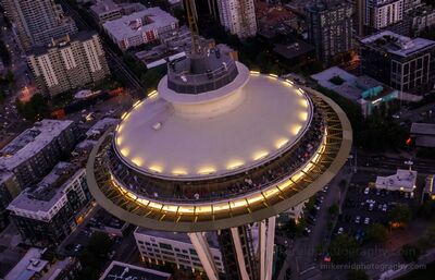 Seattle Aerial Dusk Space Needle Aerial night view of Seattle’s Space Needle illuminated against the city lights below. The glowing observation deck and soft streetlights create a striking...