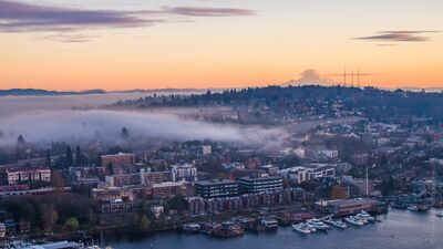 Fog Over Eastlake at Sunrise, Seattle Morning fog drifts across Seattle’s Eastlake neighborhood and the shores of Lake Union beneath a soft pastel sunrise. This aerial view looks across the city...