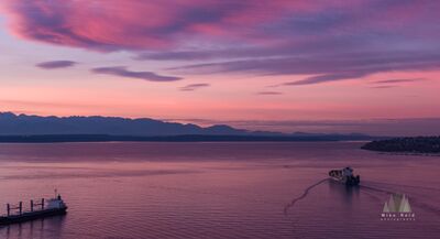 Cargo Ship on Elliott Bay at Sunset, Seattle A cargo ship heads across Elliott Bay beneath a vivid pink and purple sunset over Seattle, Washington. The Olympic Mountains form a dark silhouette beyond Puget...