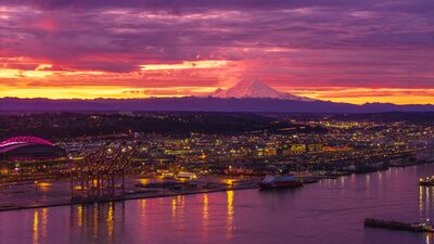 Mount Rainier Sunrise Over the Port of Seattle Mount Rainier rises beyond Seattle beneath a brilliant magenta and gold sunrise, while lights from the Port of Seattle reflect across Elliott Bay. This aerial...