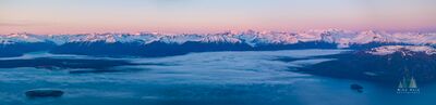 Fog Layer Beneath the Alaska Coast Range A broad layer of fog settles across the waterways and lower valleys beneath Alaska’s Coast Range, while snow-covered peaks rise into soft pink and blue evening...