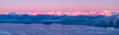 Coastal Range Alpenglow Soft pink alpenglow spreads across the snow-covered Coast Range near Petersburg, Alaska, while low clouds drift through the waterways below. Cool blue shadows...