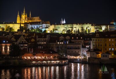 Prague Castle and Vltava River at Night A nighttime view across the Vltava River toward Prague Castle and St. Vitus Cathedral, glowing above the historic riverfront of Prague, Czech Republic. Warm...