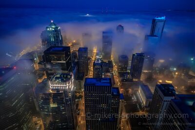 Downtown Seattle in Morning Fog from Columbia Center Low morning fog drifts through downtown Seattle, wrapping around skyscrapers while illuminated streets glow beneath the clouds. Photographed from the Columbia...
