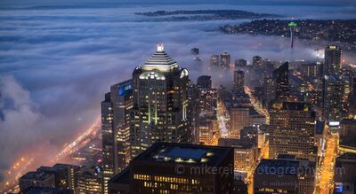 Seattle Fog Rolling Through the City at Night Low fog pours into downtown Seattle at night, wrapping the waterfront and lower city while the Space Needle rises above the cloud layer. Photographed from the...