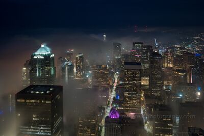 Seattle City Lights Emerging Through Night Fog Fog drifts between the towers of downtown Seattle as city lights glow through the mist, photographed from the Sky View Observatory at Columbia Center. The Space...
