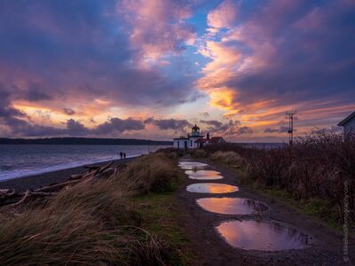 West Point Lighthouse Sunset Reflections at Discovery Park A dramatic sunset fills the sky above West Point Lighthouse at Discovery Park in Seattle, Washington. Brilliant pink, violet, and golden clouds stretch across...
