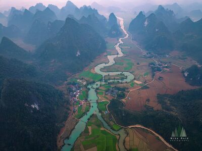 Winding River Through Phong Nam Valley at Sunrise Aerial view across Phong Nam in Cao Bằng Province, northern Vietnam, where a winding river threads through patchwork farmland and small villages beneath steep...